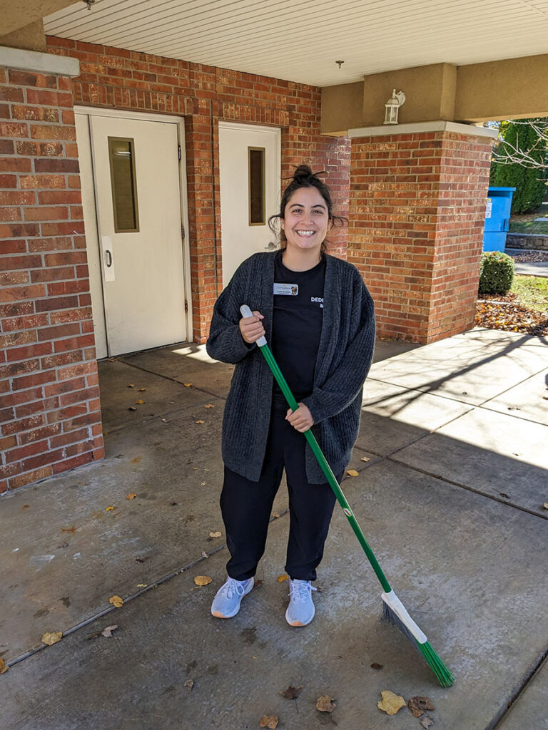 A woman sweeping outside with a broom, cleaning the sidewalk.