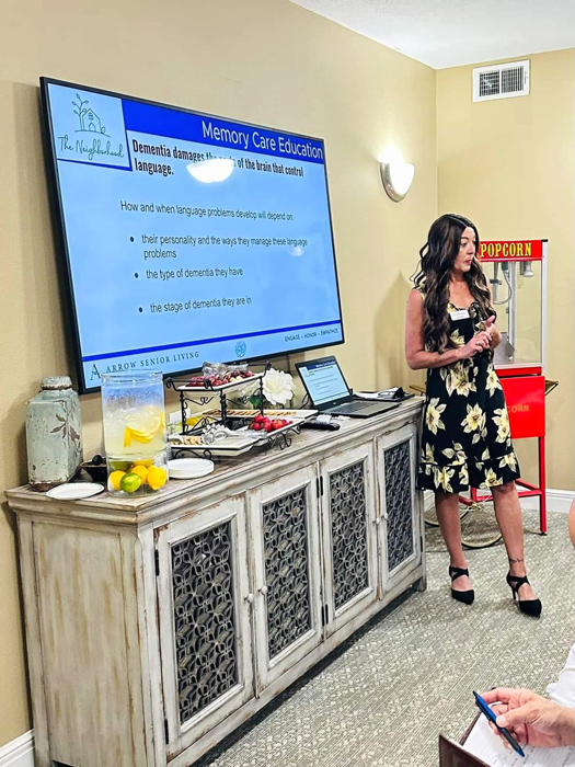 Memory Care Education session focusing on language and dementia. The instructor stands near the presentation screen and refreshments, with a popcorn machine in the background.