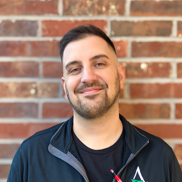 Anthony Argenta, Director of Wellness at The Fremont Senior Living, smiles confidently against a brick wall, reflecting his dedication to resident care and well-being.