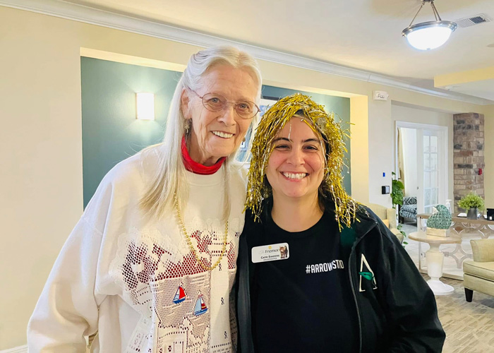 Senior resident and team member smile brightly during a Mardi Gras celebration, with festive gold tinsel and community pride on full display.