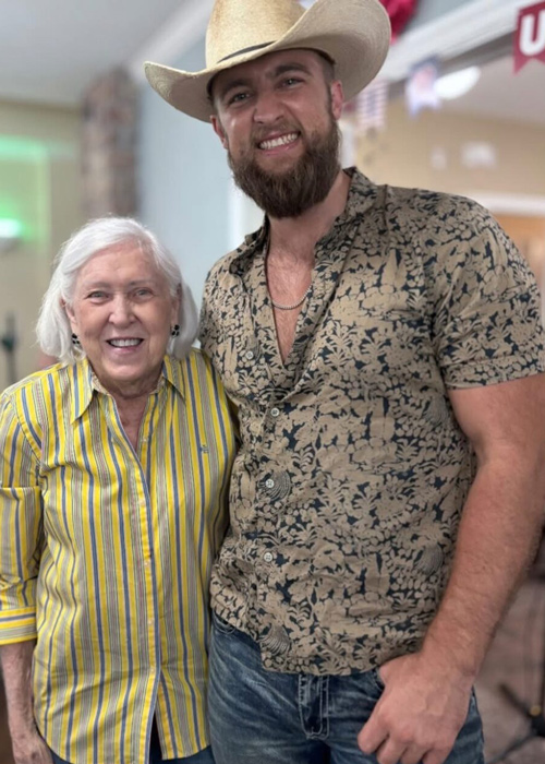 A smiling senior woman stands beside a cowboy-hat-wearing guest, enjoying a Western-themed celebration at The Fremont Senior Living.