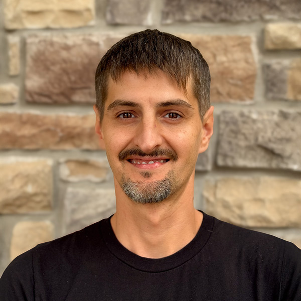 Wyatt Koory, Plant Operations Director at The Fremont Senior Living, smiling in a professional headshot. He has short brown hair, a trimmed goatee, and wears a black shirt, standing in front of a stone wall background.