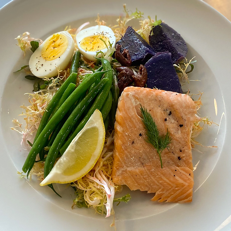 A chef-prepared dish of fresh greens, salmon, purple sweet potato, green beans and eggs.