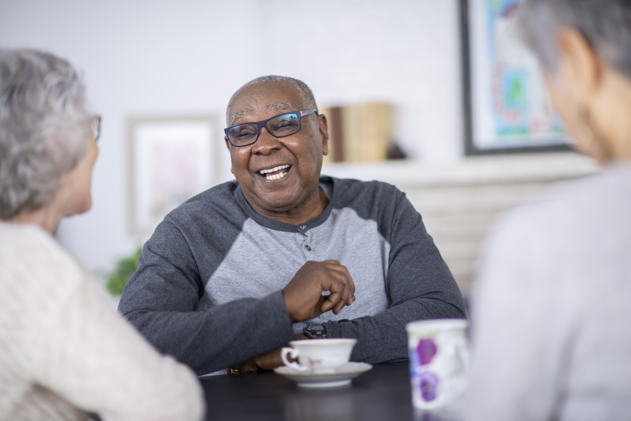 Senior resident smiling and laughing while seated at a table, enjoying conversation with peers over coffee in a bright, welcoming community dining space.