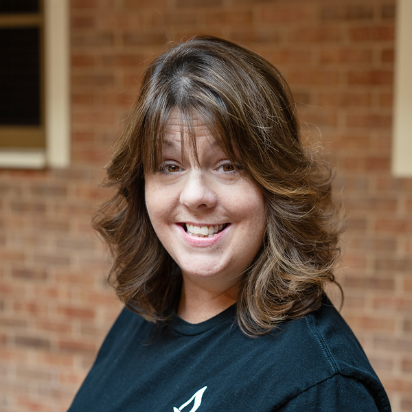 Christina Patterson, Resident Services Director at The Fremont Senior Living, smiling in a professional outdoor headshot with shoulder-length wavy brown hair, a black top, and a softly blurred brick background.